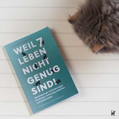 Katze betrachtet Buch "Weil 7 Leben nicht genug sind!"